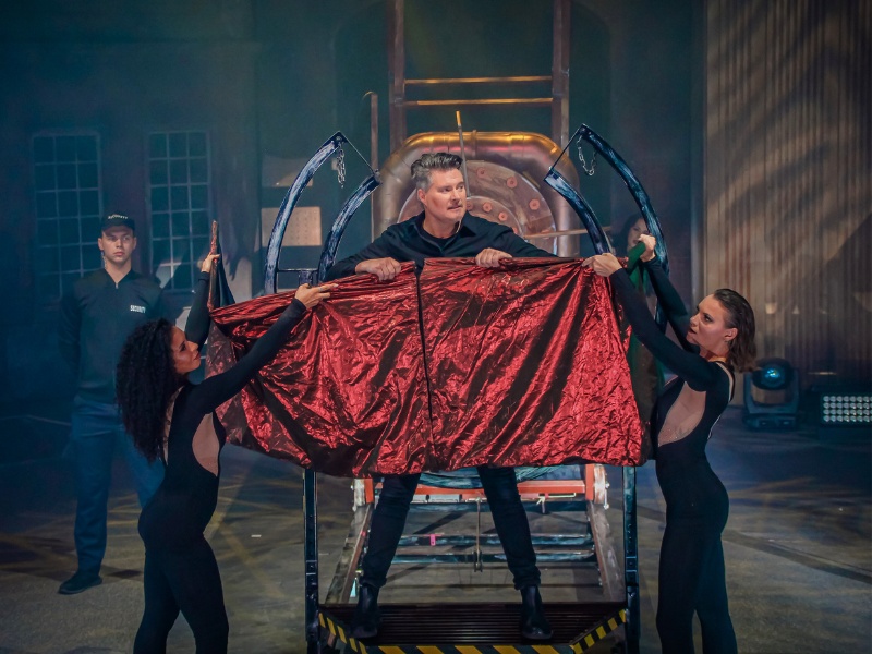 People on a stage, posing for a scene. The person in the center is half covered by a red cloak.